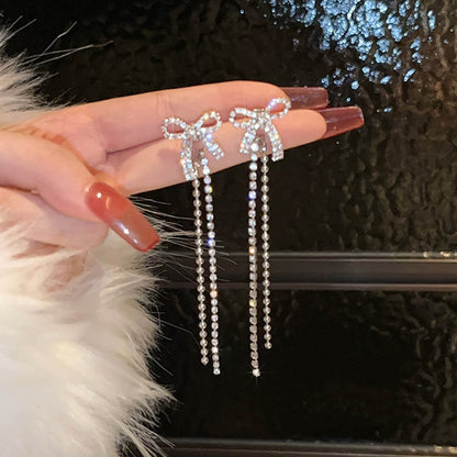 A pair of bow tassel earrings and silver needles.